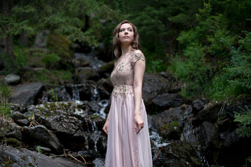 A young woman in a long dress on the background of a mountain waterfall. Enjoyment of nature.