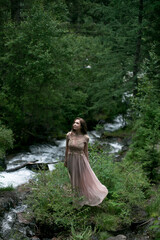 A young woman in a long dress on the background of a mountain waterfall. Enjoyment of nature.