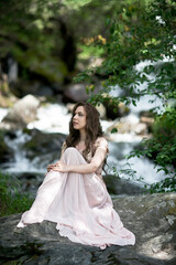 Fototapeta na wymiar A young woman in a long dress on the background of a mountain waterfall. Enjoyment of nature.