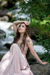 A young woman in a long dress on the background of a mountain waterfall. Enjoyment of nature.