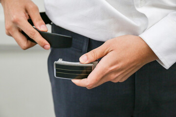 The groom tightens his belt. A man holding his hands on his belt. Morning wedding preparation.