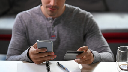Young man sitting in living room and shopping online on smart phone.
