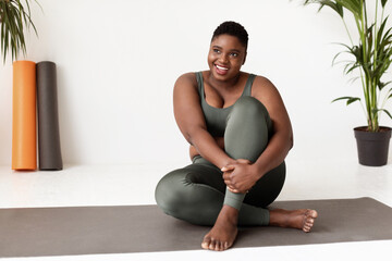 Positive african american lady plus size sitting on yoga mat - Powered by Adobe