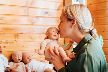 Portrait pretty caucasian young woman kissing realistic newborn baby doll sitting near collection...