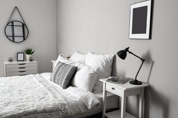 Comfortable bed and table with lamp near light wall