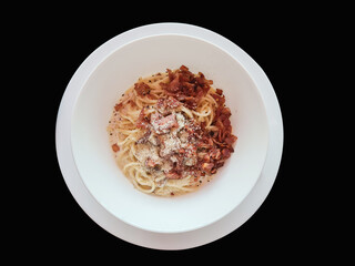 Bacon spaghetti with white sauce in a plate on isolated black background
