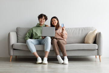 Online shopping. Asian couple sitting on couch at home, using laptop and credit card, purchasing...