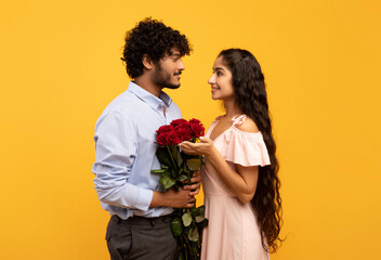 Romantic indian spouses holding bouquet of flowers and looking at each other, guy pampering his...