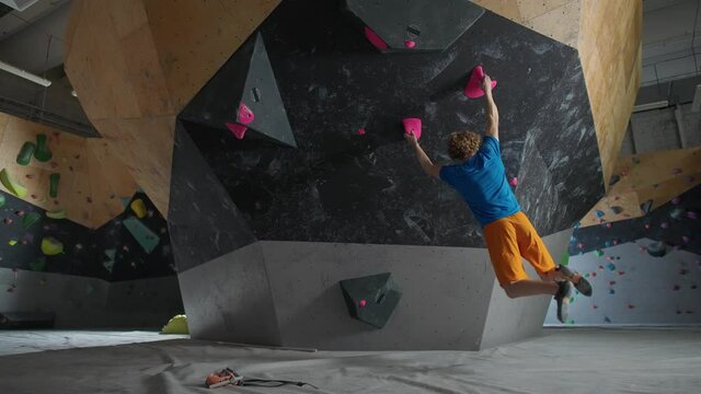 Young climber training on a climbing wall, practicing rock-climbing and moving up.