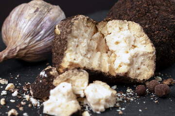 side view of a whole and broken ball of Belper Knoll cheese, black pepper and garlic lying on a black slate board. Hard Swiss cheese in the form of small balls in a sprinkle of black pepper. Close-up