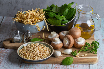 Ingredients for Rustic Mushroom Spinach Pasta. Mushrooms, spinach, garlic clove, pine nuts, spices and parsley on a wooden background