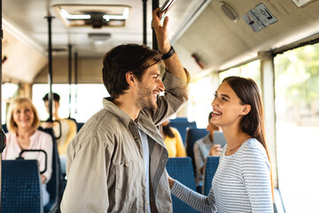 Beautiful smiling couple standing in bus and talking - obrazy, fototapety, plakaty