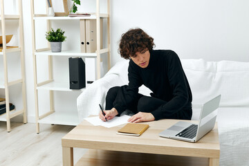 Fototapeta premium curly guy sitting on the couch at the table in front of a laptop living room