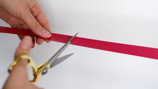 Hand with scissors cutting red ribbon opening ceremony concept. Isolated on white background