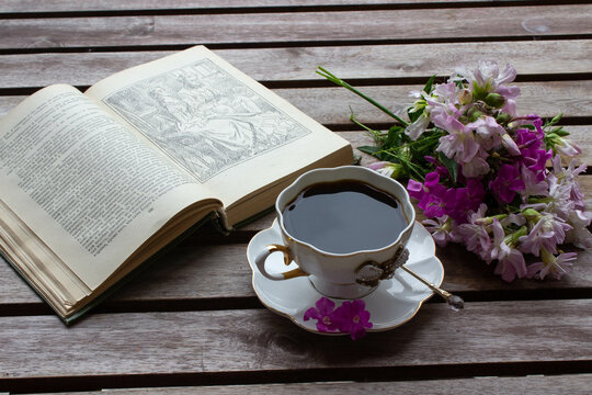 Spring still life scene. Artistic composition with cup of hot aromatic morning coffee and Floral composition. Vintage feminine styled photo. Russian breakfast with book.