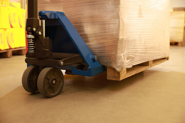 Manual forklift with wrapped pallets in warehouse, closeup. Logistics concept
