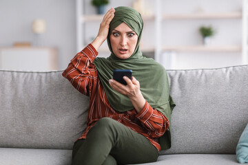 Shocked Muslim Woman Holding Smartphone Touching Head At Home