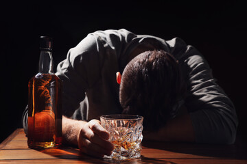 Addicted man with glass of alcoholic drink at wooden table against black background