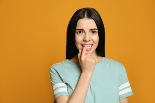 Young Woman Biting Her Nails On Yellow Background