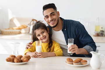 Obraz na płótnie Canvas Positive middle eastern dad and daughter enjoying snacks in kitchen