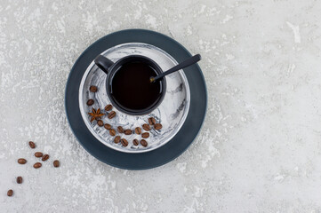 a dark ceramic cup with expresso on a plaster tray with coffee beans stands on a gray concrete...
