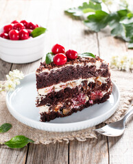 A slice of black chocolate sponge cake with cherry on a wooden table