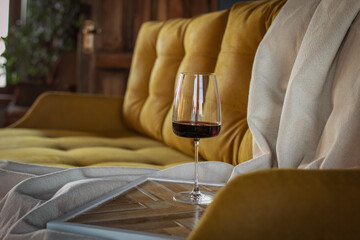 A glass of red wine is on the table backgrounded by yellow sofa