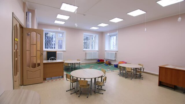 Teacher desk small round children tables and soft carpet with toys in spacious play room of new kindergarten premise