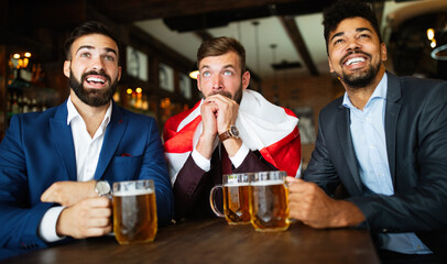 Men fans screaming and watching football on TV and drink beer in a pub