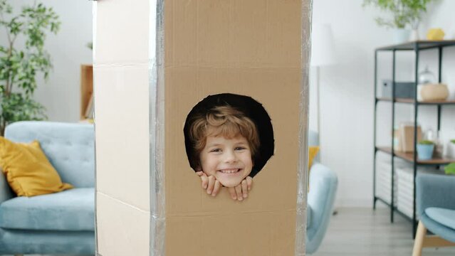 Slow motion portrait of adorable blond child smiling from cardboard spaceship looking at camera at home. Childhood and kid concept.