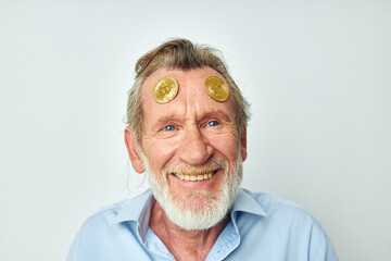 Portrait elderly man in a blue shirt bitcoins on the face light background