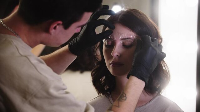 Eyebrow lamination - an eyebrow specialist applying wrapping on the brow of his female client