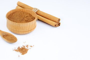 Ground cinnamon in a wooden bowl and cinnamon sticks.