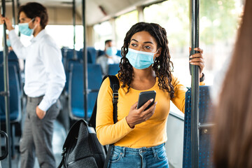 Beautiful black woman in face mask using phone in bus