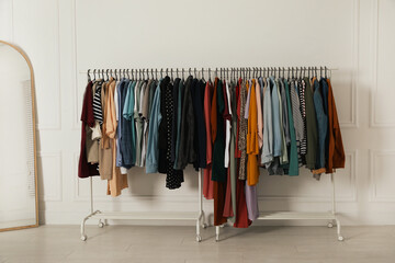 Racks with stylish clothes and mirror near white wall indoors. Fast fashion
