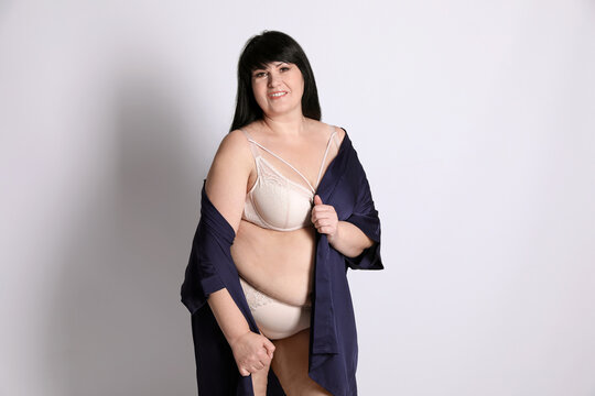 Beautiful overweight woman in beige underwear and silk robe on light background. Plus-size model