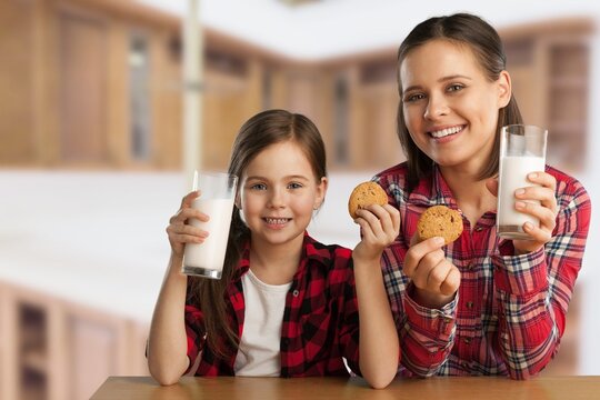 Pretty Girl Drinking Milk With Her Mom And Eating Cookies, Sitting At The Kitchen