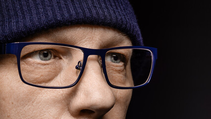 The face of a middle-aged man with glasses and a knitted hat. Close-up macro photo, black background.