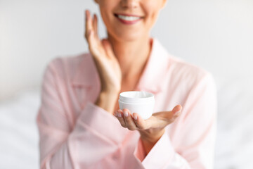 Closeup of smiling woman holding showing cream jar