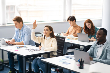 Portrait of smiling female student raising hand at classroom