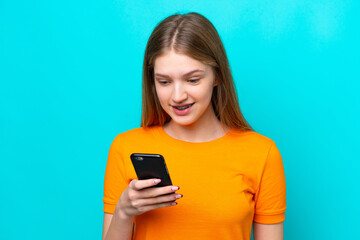 Teenager Russian girl isolated on blue background sending a message or email with the mobile