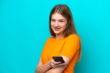 Teenager Russian girl isolated on blue background holding a mobile phone and with arms crossed