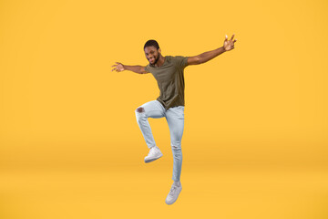 Fototapeta na wymiar Happy african american guy jumping up over yellow background, full-length portrait, free space
