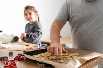 Cropped view of unrecognizable man and his daughter making sweets with biscuit cutters on processing board. Father putting cookies on the baking sheet