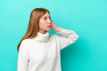 Fototapeta premium Young redhead woman isolated on blue background listening to something by putting hand on the ear