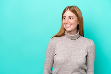 Young redhead woman isolated on blue background looking to the side and smiling