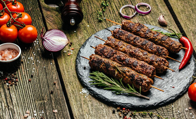 Lula kebab, traditional Caucasian dish. On the black background of the concrete, on a chopping board, with ketchup, spices and tomatoes copy space above
