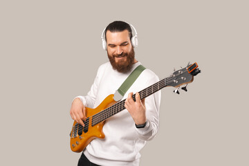 Photo of young handsome bearded man playing at bass guitar with 5 strings.