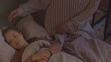 Slowmo shot of loving mother in striped pajamas kissing her sleeping daughter goodnight
