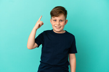 Little redhead boy isolated on blue background intending to realizes the solution while lifting a finger up